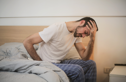 Man in pajamas sitting on edge of bed resting his forehead in his hand